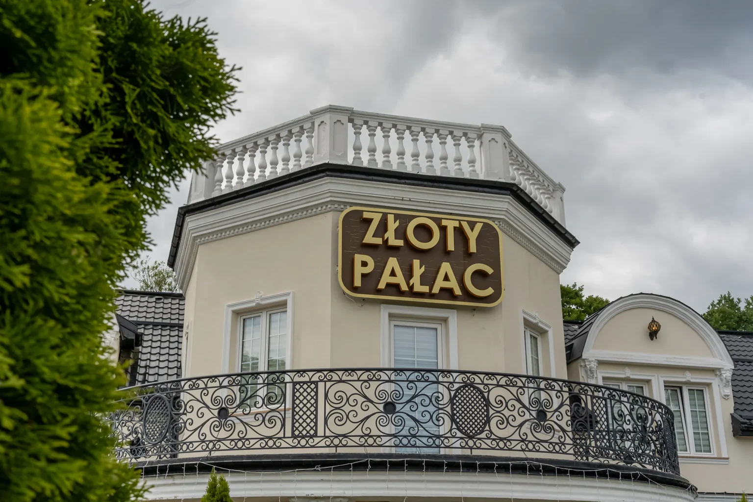 Zbliżenie na złoty szyld Złotego Pałacu i kuty balkon z balustradą